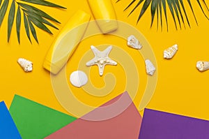 Yellow bottles of sunscreen cream, tropical palm leaves, shells, starfish on colorful background top view flat lay copy space. Sun