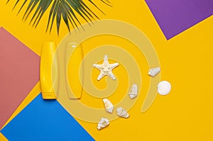Yellow bottles of sunscreen cream, tropical palm leaves, shells, starfish on colorful background top view flat lay copy space. Sun