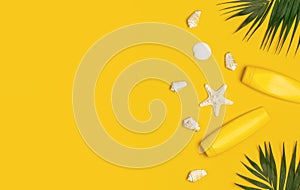 Yellow bottles of sunscreen cream, tropical palm leaves, shells, starfish on yellow background top view flat lay copy space. Sun