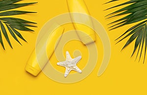 Yellow bottles of sunscreen cream, tropical palm leaves, shells, starfish on yellow background top view flat lay copy space. Sun