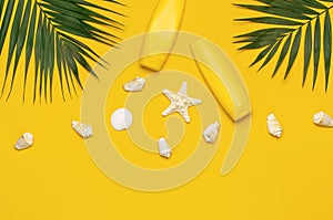 Yellow bottles of sunscreen cream, tropical palm leaves, shells, starfish on yellow background top view flat lay copy space. Sun