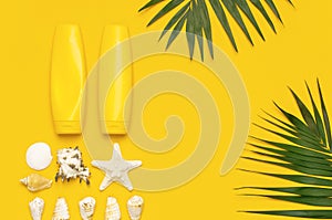 Yellow bottles of sunscreen cream, tropical palm leaves, shells, starfish on yellow background top view flat lay copy space. Sun