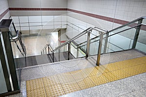 Yellow braille block tile and gray marble granite stairs and stainless steel railings with clear glass partition