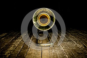 Yellow brass instrument trombone lies on the wooden floor of the stage. front view on the bell photo