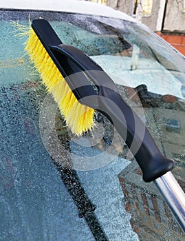 A yellow bristle brush cleans the icy windshield of a passenger car