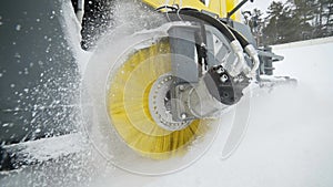 The yellow brush of snow and ice removal truck is rotating and removing snow from the road, wheeled harvesting machinery