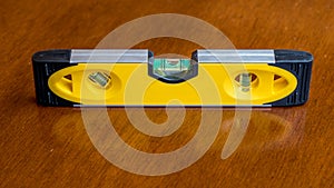 Yellow bubble level showing bubble in the level position to indicate a flat plane, resting on a brown wooden surface