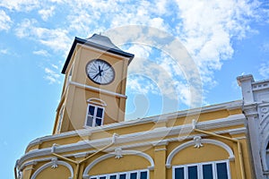 Yellow building with clock tower in Chino-Portuguese style on blue sky background, Phuket old town, Thailand photo