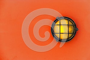 Yellow bulkhead light ship deck lamp on installed on orange color wooden wall background.