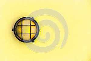 Yellow bulkhead light ship deck lamp surrounded by a metal rusted frame fixed to a painted light yellow pastel wall