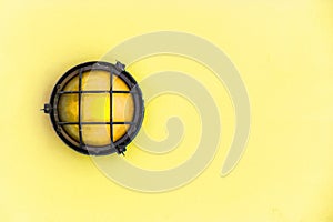 Yellow bulkhead light ship deck lamp surrounded by a metal rusted frame fixed to a painted light yellow pastel wall photo