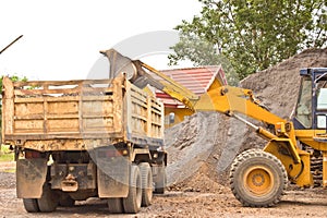 Yellow bulldozer was scooping soil into the truck.