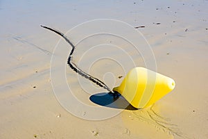 A yellow buoy and its anchorage chain lying on the wet sand under a bright sunshine