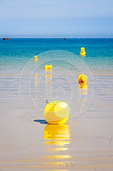 Yellow buoys lying on the wet sand and floating on the sea along the beach under a bright sunshine