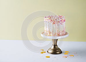 Yellow buttercream ombre birthday cake with colorful sprinkles over yellow background with copy space. Romantic love concept.