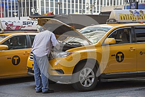 Yellow cab driver looking at engine of his taxi