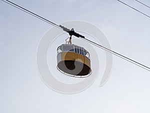 Yellow cabin in retro style riding on the cable car against the background of a cloudy sky