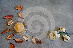 Yellow candle with dry petals and white flowers on a gray background