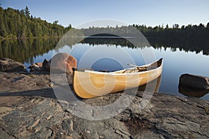 Yellow canoe on rocky shore of calm lake with pine trees