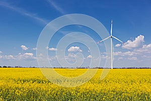 In the yellow canola field stands a white turbogenerator, against the sky with clouds, the concept