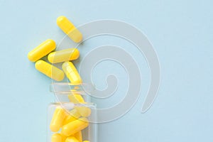 Yellow capsules from glass bottle on blue background. copyspace for text. Epidemic, painkillers, healthcare, treatment pills and
