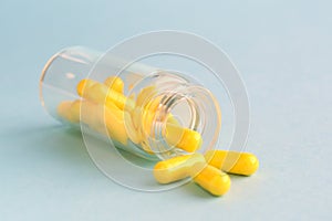 Yellow capsules from glass bottle on blue background. copyspace for text. Epidemic, painkillers, healthcare, treatment pills and