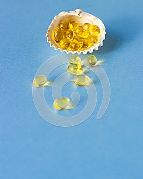 Yellow capsules with oil fish oil, omega 3, omega 6, omega 9, vitamin A, vitamin D, vitamin D3, vitamin E in a conch on a blue p