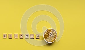 Yellow capsules in the round bowl and the word vitamin D from wooden cubes