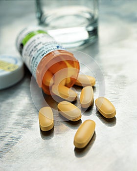 Yellow capsules spilling from prescription medication bottle with glass of water photo