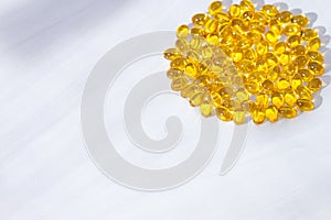 Yellow capsules with vitamin D, fish oil omega 3 with sunlight on white wooden background. Healthy and medical concept