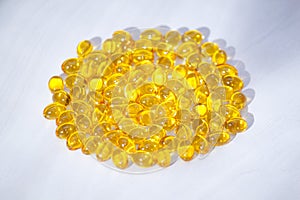 Yellow capsules with vitamin D, fish oil omega 3 with sunlight on white wooden background. Healthy and medical concept