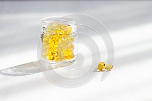 Yellow capsules with vitamin D, fish oil omega 3 with sunlight on white wooden background. Healthy and medical concept