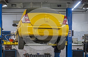 A yellow car being repaired hangs on a lift in a car repair shop