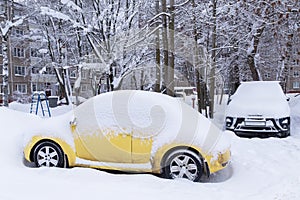 Yellow car covered snow after heavy snowfall and blizzard on town street