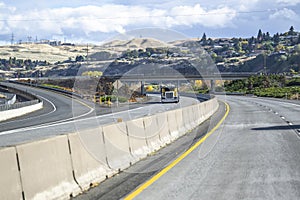 Yellow car hauler big rig semi truck with empty semi trailer running on the highway with overpass road intersections