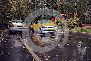 Yellow car rides in the yard on a wet road in the rain . Beautiful splashes of water from under the wheels.