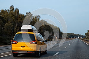 The yellow car with rooftop cargo carriers is driving along the summer