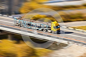 Yellow car transporter moving fast at the bridge