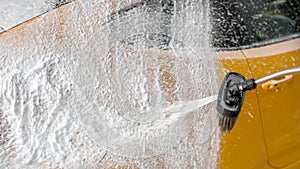 Yellow car washed at carwash - white thick foam and shampoo splutter on the rear side. Space for text on left.