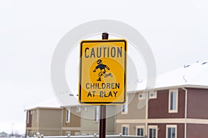 Yellow Caution Children At Play sign against blurry building and cloudy sky