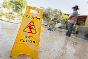 Yellow caution sign and blur of man doing floor polishing