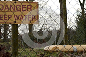 Yellow caution sign with the meesage of Danger, Deep Water behind the metal fence in the forest