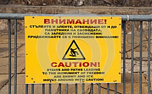 Yellow caution sign near The Liberty Memorial, also known as the Shipka Monument in Bulgaria.