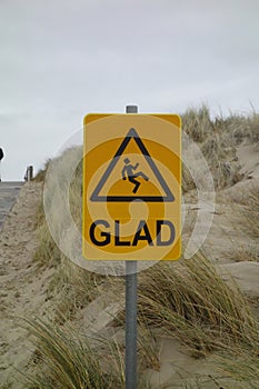 Yellow caution sign with the word "Glad" written on it on the beach