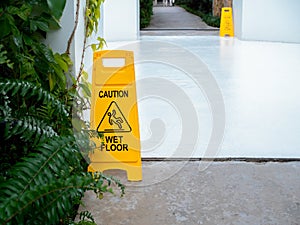 Yellow caution slippery wet floor sign with slippery person warning icon on wet white concrete floor background.