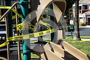 Yellow caution tape in english and spanish barring access to playground equipment at a park due to coronavirus photo