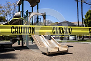 Yellow caution tape in english and spanish barring access to playground equipment at a park due to coronavirus