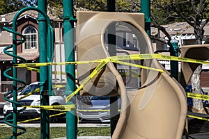 Yellow caution tape in english and spanish barring access to playground equipment at a park due to coronavirus quarantine