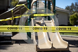 Yellow caution tape stating COVID-19 denying access to playgound equipment at a park photo