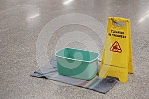 Yellow Caution wet floor cleaning in progress sign on wet floor with green bucket